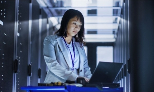 Asian Female IT Engineer Working on a Laptop in a Big Data Center Full of Rack Servers 