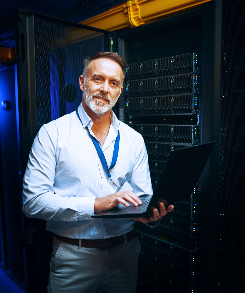 A Cybersecurity professional works on his laptop in the server room. A Cybersecurity professional works on his laptop in the server room.