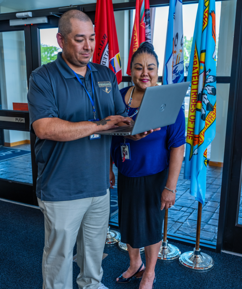 Colleagues stand in front of flags looking at a laptop