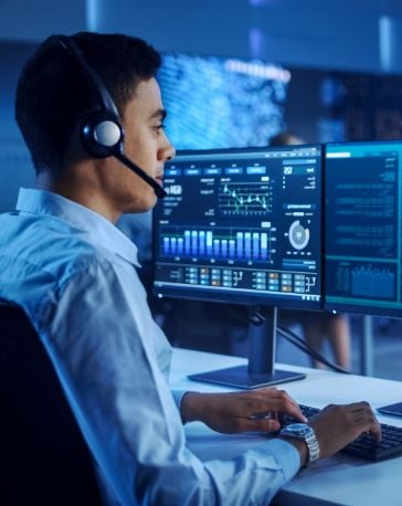 Confident Male Data Scientist Works on Personal Computer Wearing a Headset in Big Infrastructure Control and Monitoring Room