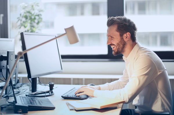 Businessman on smiling while on video conference desktop computer-600x398