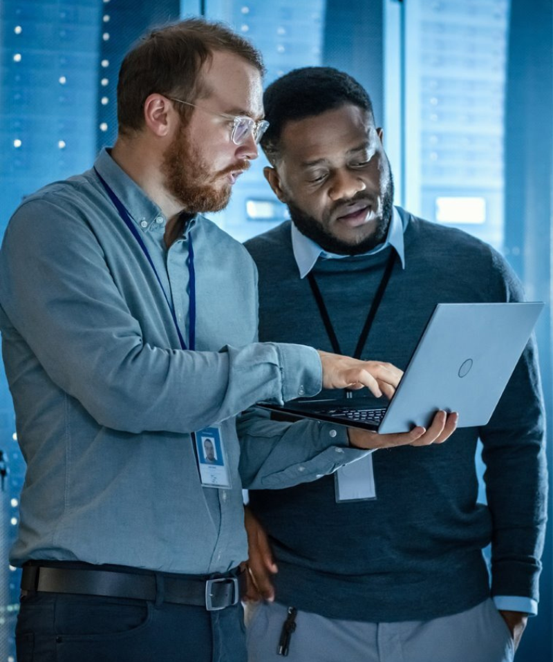 Men in server room looking at laptop - 800 x 958px