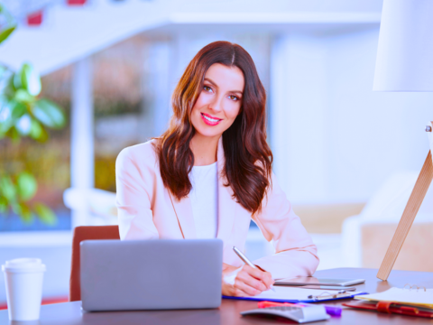 An administrative professional sits at her desk with her laptop writing notes.