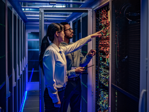 IT professionals are in the server room looking at cables in a rack together.