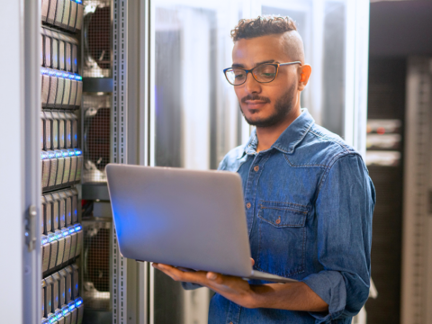 A male IT Professional works on his laptop in the server room.