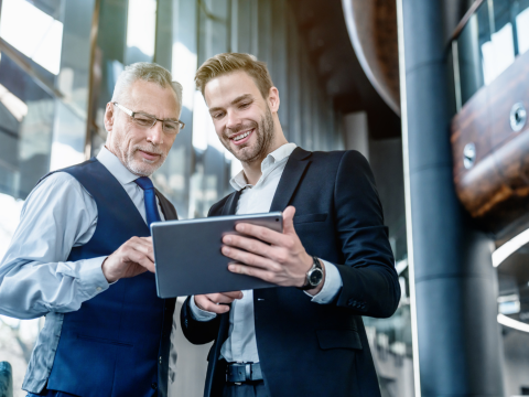 Two businessmen collaborate while viewing information on a tablet